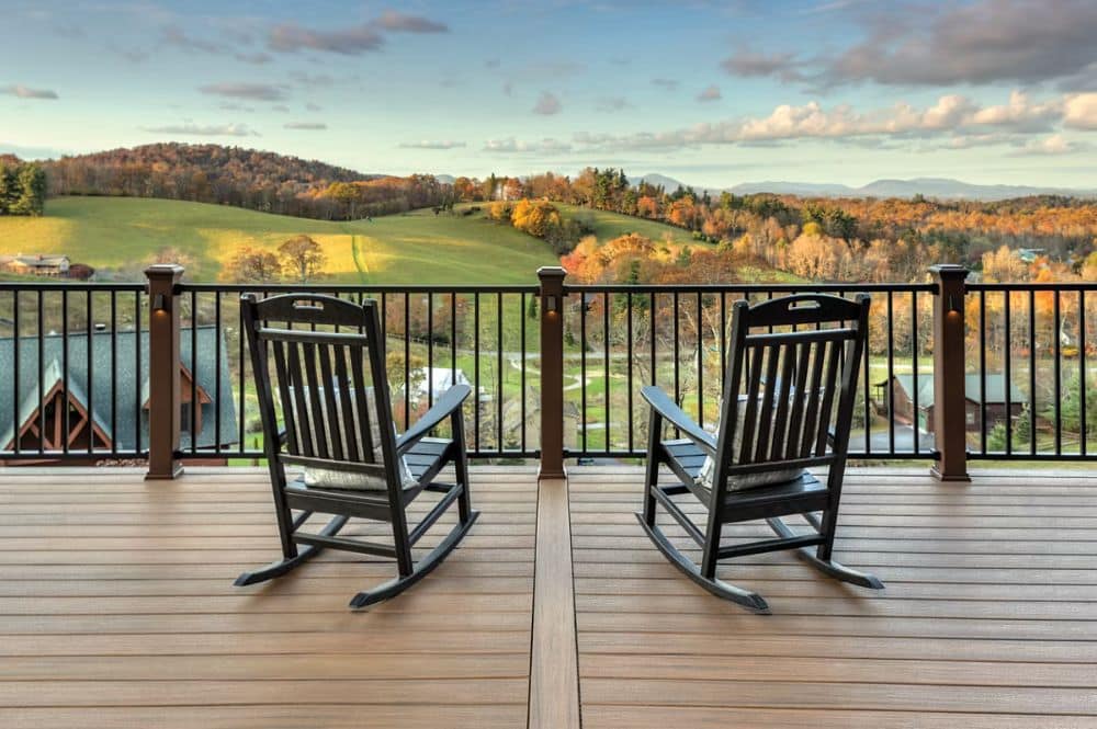 Two wooden rocking chairs on a deck, offering a serene view of a picturesque valley.