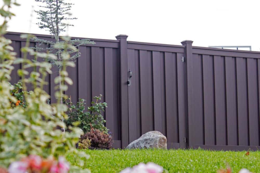 A brown fence adorned with colorful flowers and green grass, exemplifying landscaping with fences.