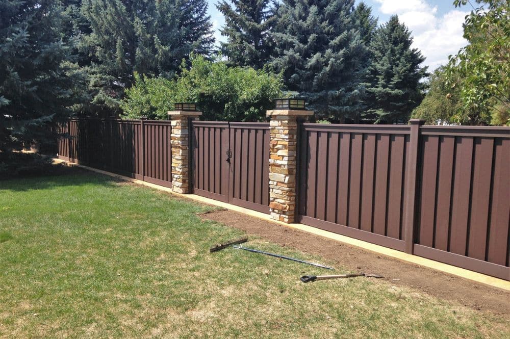 a newly installed Trex composite fence with stone pillars lines a backyard showcasing the options Trex backyard fencing offers.